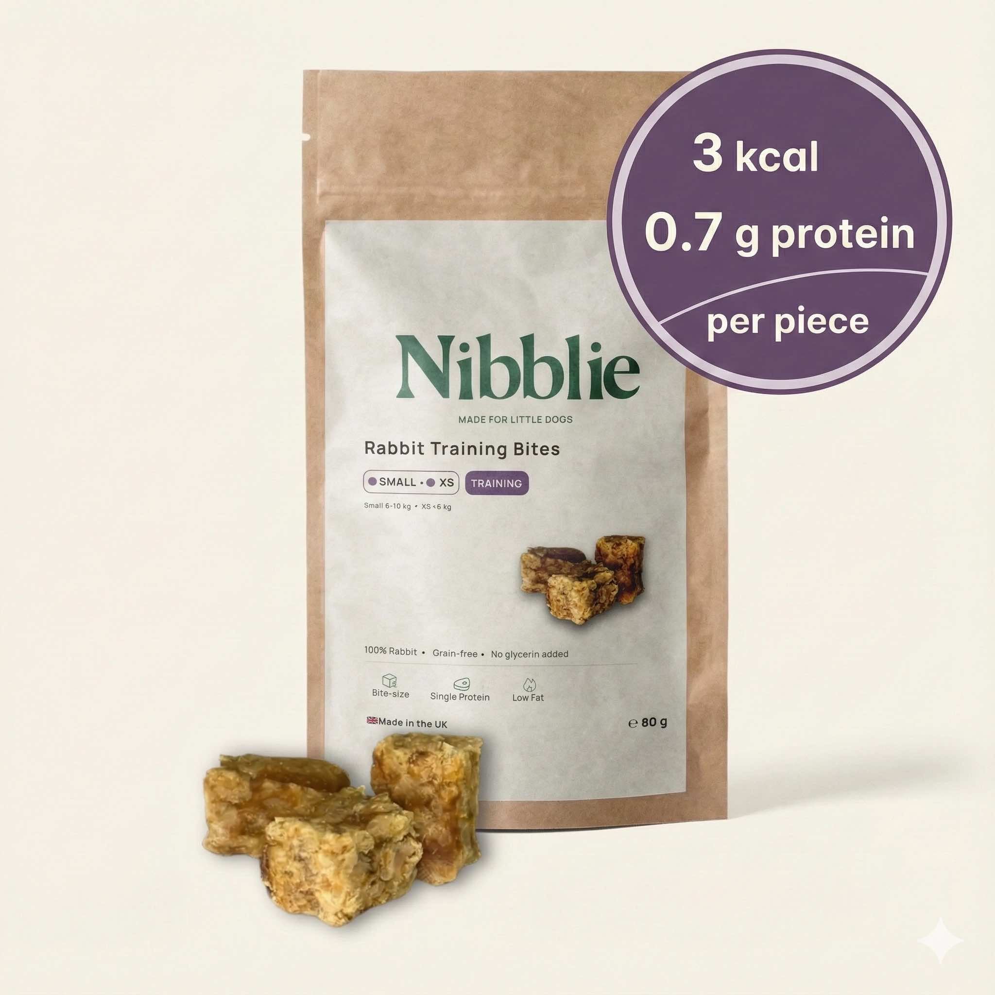 Nibblie Rabbit Training Bites 80g pack on warm linen with bites in front; single-protein , low-cal training treats for small dogs.