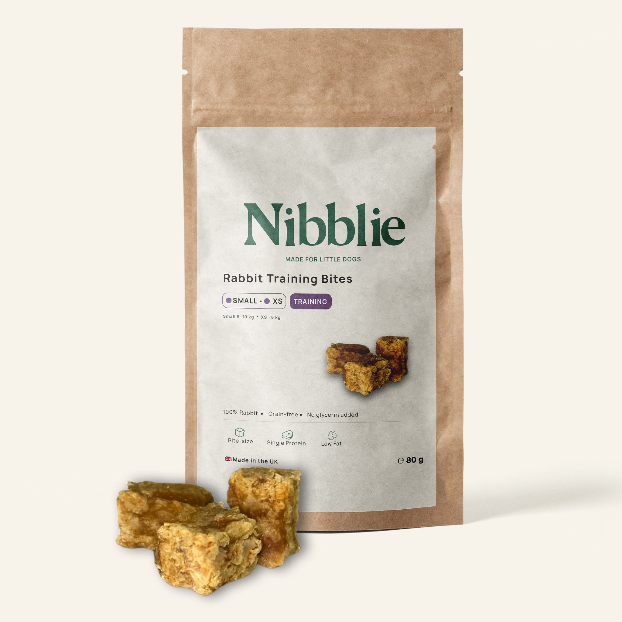 Nibblie Rabbit Training Bites 80g pack on warm linen with bites in front; single-protein training treats for small dogs.