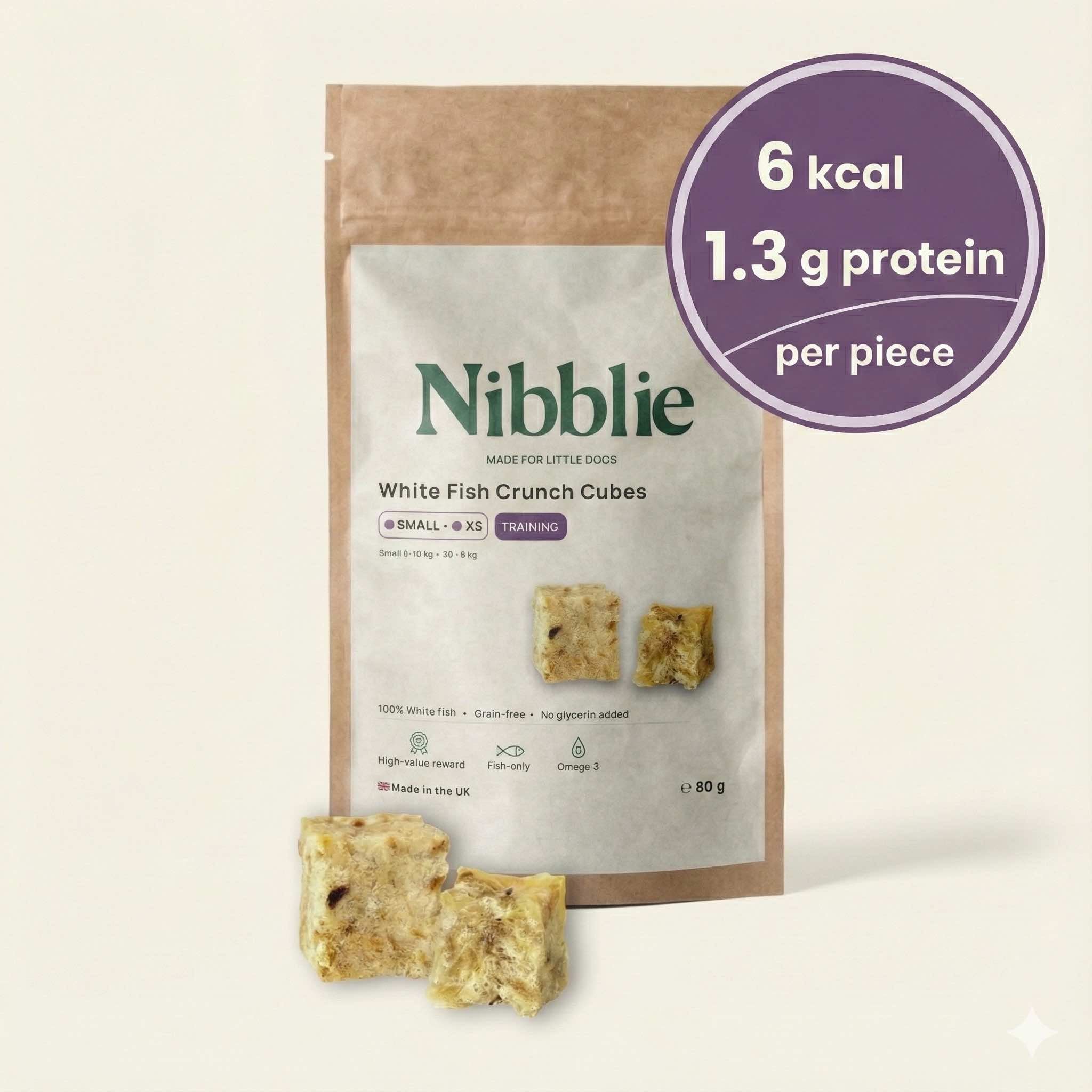 Nibblie White Fish Crunch Cubes 80g pack on warm linen with cubes in front; natural, low-cal, air-dried white-fish treats.
